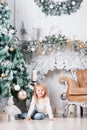 Adorable little blonde girl in a blue jeans sitting on a floor near christmas tree and looking on toy. Royalty Free Stock Photo