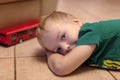 Adorable little boy with blue eyes lays on the ceramic floor with toy red bus. Blonde hair, green t-shirt.