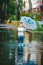 Adorable little boy holding colorful umbrella standing in a puddle on warm summer day