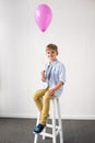 adorable little boy holding pink balloon while sitting in stool at birthday Royalty Free Stock Photo