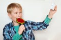 Adorable little boy licking big colorful lollipop and making selfie by his smart phone isolated on white background. Fashionable k Royalty Free Stock Photo