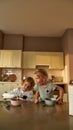 Adorable little boy pouring milk into a bowl of cereal while preparing breakfast, sitting together with his sister at Royalty Free Stock Photo