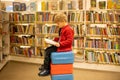 Adorable little boy, sitting in library, reading book and choosing what to lend, kid in book store Royalty Free Stock Photo