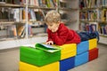 Adorable little boy, sitting in library, reading book and choosing what to lend, kid in book store