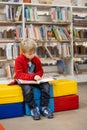 Adorable little boy, sitting in library, reading book and choosing what to lend, kid in book store Royalty Free Stock Photo