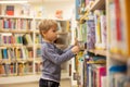 Adorable little boy, sitting in library, reading book and choosing what to lend, kid in book store Royalty Free Stock Photo