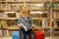 Adorable little boy, sitting in library, reading book and choosing what to lend, kid in book store Royalty Free Stock Photo