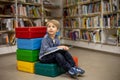 Adorable little boy, sitting in library, reading book and choosing what to lend, kid in book store Royalty Free Stock Photo