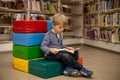 Adorable little boy, sitting in library, reading book and choosing what to lend, kid in book store Royalty Free Stock Photo