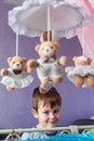 Adorable little boy standing near cot with Baby music mobile carousel. Big Brother watches younger sister in crib