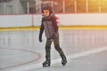 Adorable little boy in winter clothes with protections skating o