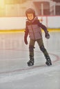 Adorable little boy in winter clothes with protections skating o