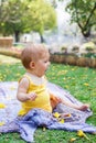 Adorable little Caucasian girl is playing with yellow flowers on a plaid at summer in park. Cute sleepy child Royalty Free Stock Photo