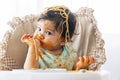 Adorable little child funny girl eating spaghetti with spoon while sitting in high-powered chair at home. Toddler child with Royalty Free Stock Photo