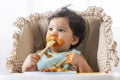 Adorable little child funny girl eating spaghetti with spoon while sitting in high-powered chair at home. Toddler child with Royalty Free Stock Photo