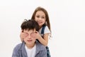 Adorable little child girl closing her brother's eyes with her hands, gently hugging him, isolated over white