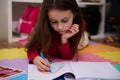 Adorable little child girl drawing rainbow with pastel pencils, lying on a multicolored puzzle carpet in her room at Royalty Free Stock Photo