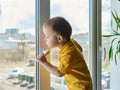 Kid stands at home on window and looks out the window at street through glass