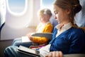 Adorable little children traveling by an airplane. Girl sitting by aircraft window and reading her ebook during the flight. Travel Royalty Free Stock Photo