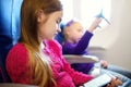 Adorable little children traveling by an airplane. Girl sitting by aircraft window and reading her ebook during the flight. Travel Royalty Free Stock Photo