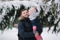 Adorable little daughter with her lovely dad stand by the big snowy tree. Cute little girl laughs and kiss her dad in Royalty Free Stock Photo