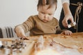 Adorable little daughter with mother making together christmas gingerbread cookies on messy wooden table. Cute toddler girl helps Royalty Free Stock Photo