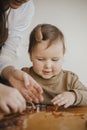 Adorable little daughter with mother making together christmas gingerbread cookies on messy wooden table. Cute toddler girl helps Royalty Free Stock Photo