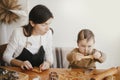 Adorable little daughter with mother making together christmas gingerbread cookies on messy wooden table. Cute toddler girl helps Royalty Free Stock Photo