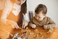 Adorable little daughter with mother making together christmas gingerbread cookies on messy wooden table. Cute toddler girl helps Royalty Free Stock Photo