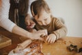 Adorable little daughter and mother making together gingerbread cookies on messy wooden table in modern room. Cute toddler girl Royalty Free Stock Photo