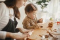 Adorable little daughter and mother making together gingerbread cookies on messy wooden table in modern room. Cute toddler girl Royalty Free Stock Photo