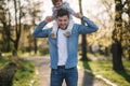 Adorable little daughter sitting on dad`s neck and laughing. Young father walk with his cute daughter in the park