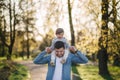 Adorable little daughter sitting on dad`s neck and laughing. Young father walk with his cute daughter in the park