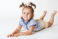 Adorable little female kid with attractive look, dreamy expression, has two funny pony tails, raises legs upwards, focused on some Royalty Free Stock Photo