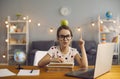 Adorable little girl with apple on her head and heap of books pointing up in front of laptop computer at home Royalty Free Stock Photo