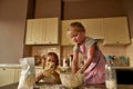 Adorable little girl in apron kneading dough while making cookies together with her brother on the kitchen table at home Royalty Free Stock Photo