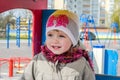 Adorable little girl baby with beautiful eyes, playing on a wooden swing at the amusement park, dressed in a raincoat with a hood, Royalty Free Stock Photo