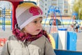 Adorable little girl baby with beautiful eyes, playing on a wooden swing at the amusement park, dressed in a raincoat with a hood, Royalty Free Stock Photo