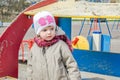 Adorable little girl baby with beautiful eyes, playing on a wooden swing at the amusement park, dressed in a raincoat with a hood, Royalty Free Stock Photo