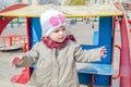 Adorable little girl baby with beautiful eyes, playing on a wooden swing at the amusement park, dressed in a raincoat with a hood, Royalty Free Stock Photo