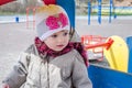 Adorable little girl baby with beautiful eyes, playing on a wooden swing at the amusement park, dressed in a raincoat with a hood, Royalty Free Stock Photo