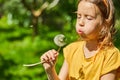 Adorable little girl blowing on a dandelion on a sunny summer day