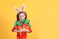 Adorable little girl with bunny ears and handful of toy carrots on orange background, space for text. Easter celebration