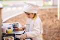 Adorable little girl in chef& x27;s coat and cap cooks at the children& x27;s toy kitchen. Playing on little kids city Royalty Free Stock Photo