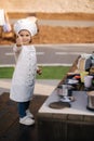 Adorable little girl in chef's coat and cap cooks at the children's toy kitchen. Playing on little kids city Royalty Free Stock Photo