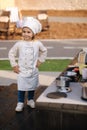 Adorable little girl in chef's coat and cap cooks at the children's toy kitchen. Playing on little kids city Royalty Free Stock Photo