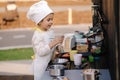 Adorable little girl in chef's coat and cap cooks at the children's toy kitchen. Playing on little kids city Royalty Free Stock Photo