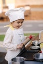 Adorable little girl in chef's coat and cap cooks at the children's toy kitchen. Playing on little kids city Royalty Free Stock Photo