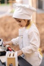 Adorable little girl in chef& x27;s coat and cap cooks at the children& x27;s toy kitchen. Playing on little kids city Royalty Free Stock Photo