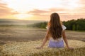 Adorable little girl child sitting on a hay rolls in a wheat field at sunset